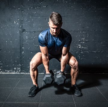 young strong fit muscular sweaty man with big muscles strength cross workout training with dumbbells weights in the gym dark image with shadows real people