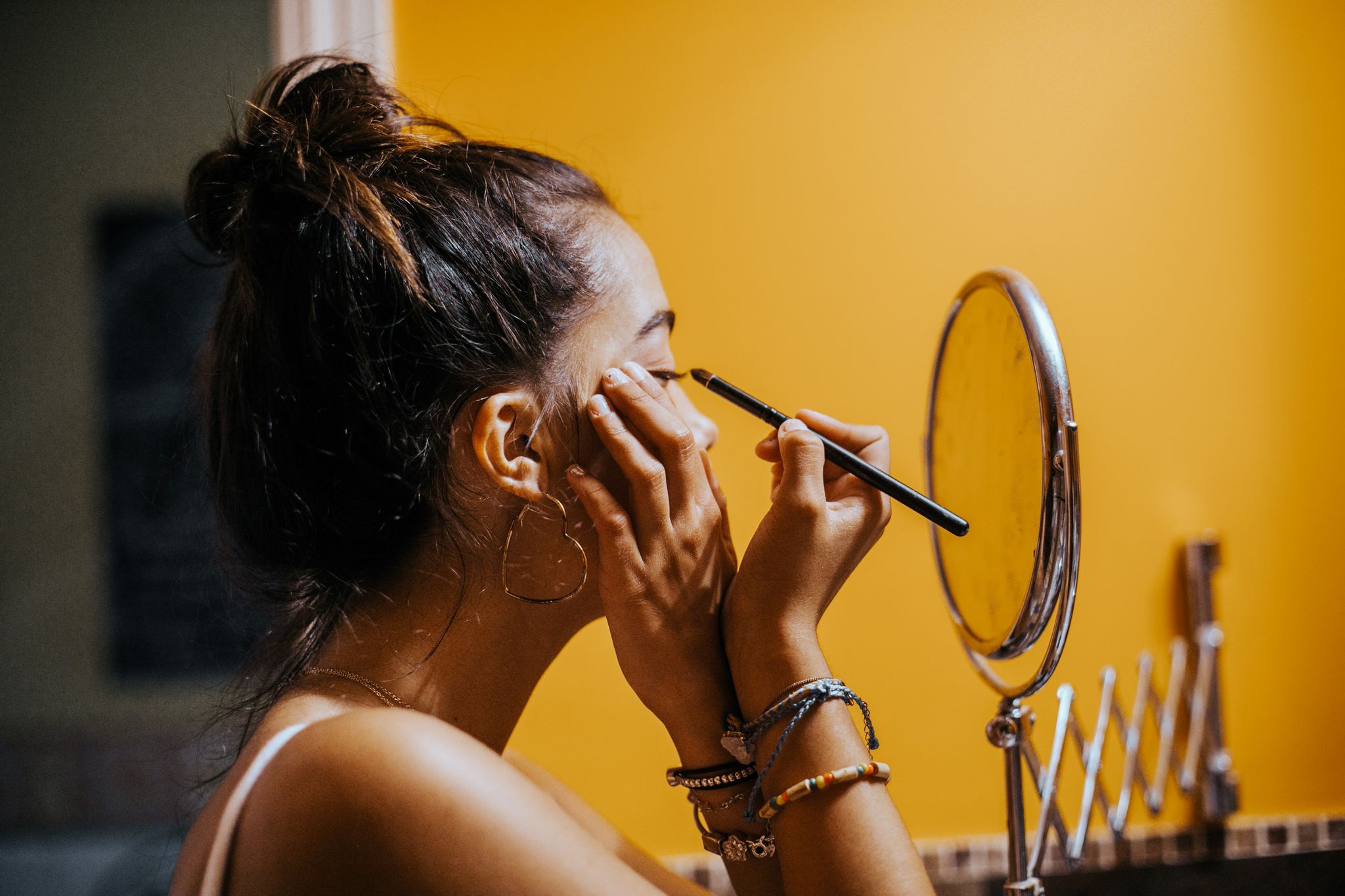 young teenager applying eyeliner in domestic bathroom