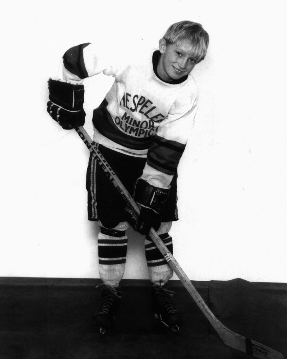a young boy smiles at the camera has he poses with his hockey stick and wears other hockey equipment