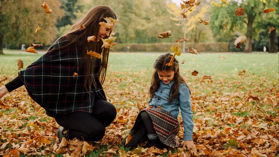 Young woman and little girl playing with autumn leaves on a meadow