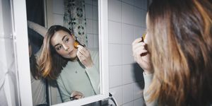 Young woman applying blush looking in mirror at college dorm bathroom