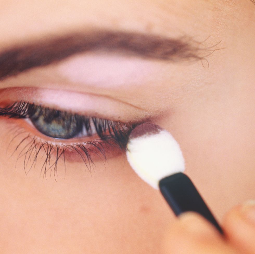 young woman applying eye make up with applicator, close up