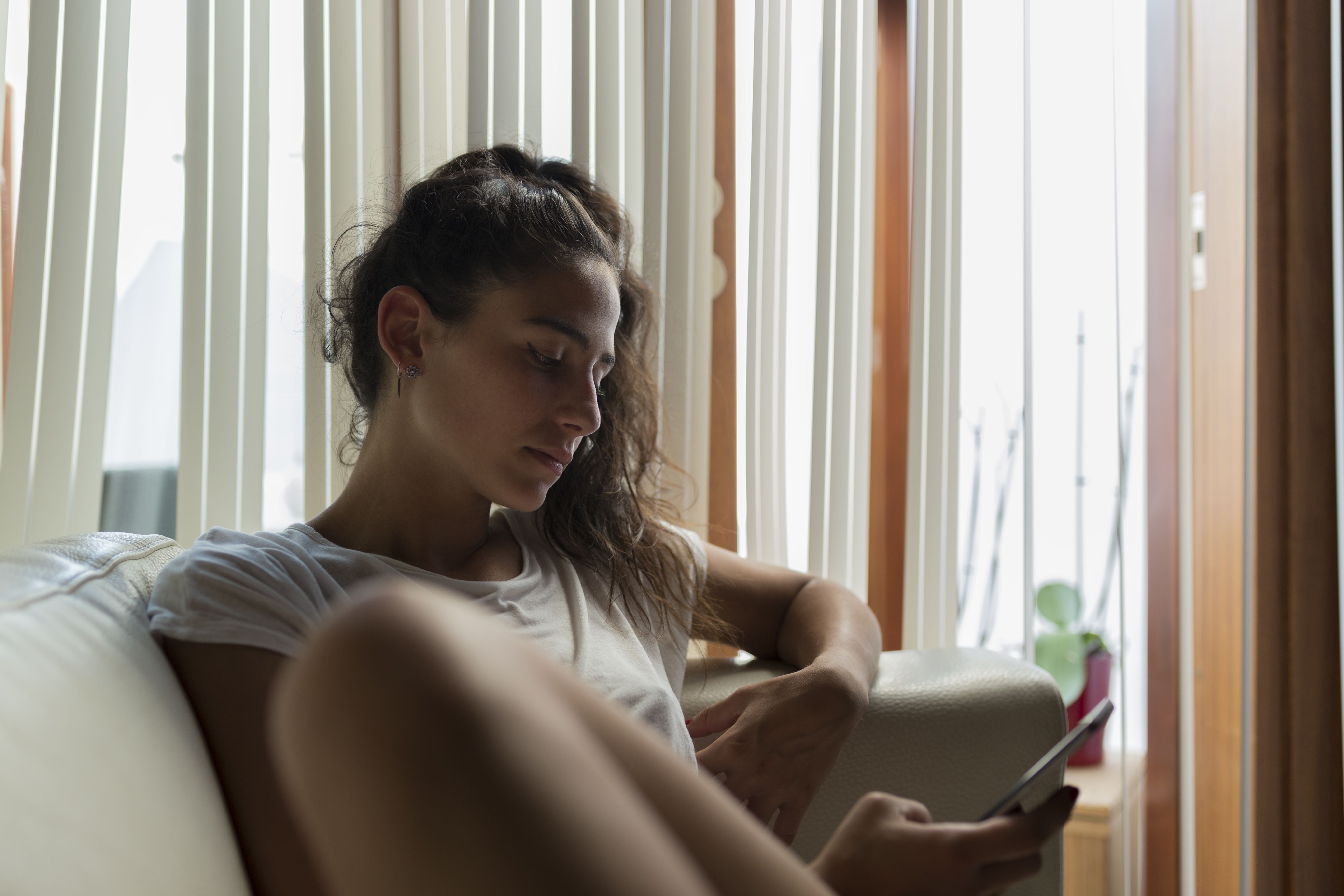 young woman at home sitting on sofa using smartphone