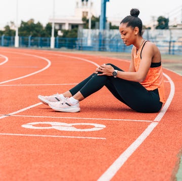 jonge vrouw zit op atletiekbaan met handen op haar knie