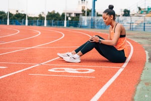 jonge vrouw zit op atletiekbaan met handen op haar knie