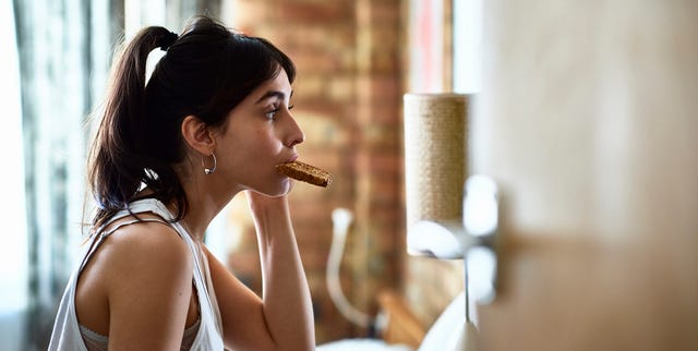 Young woman biting piece of toast and checking herself in mirror