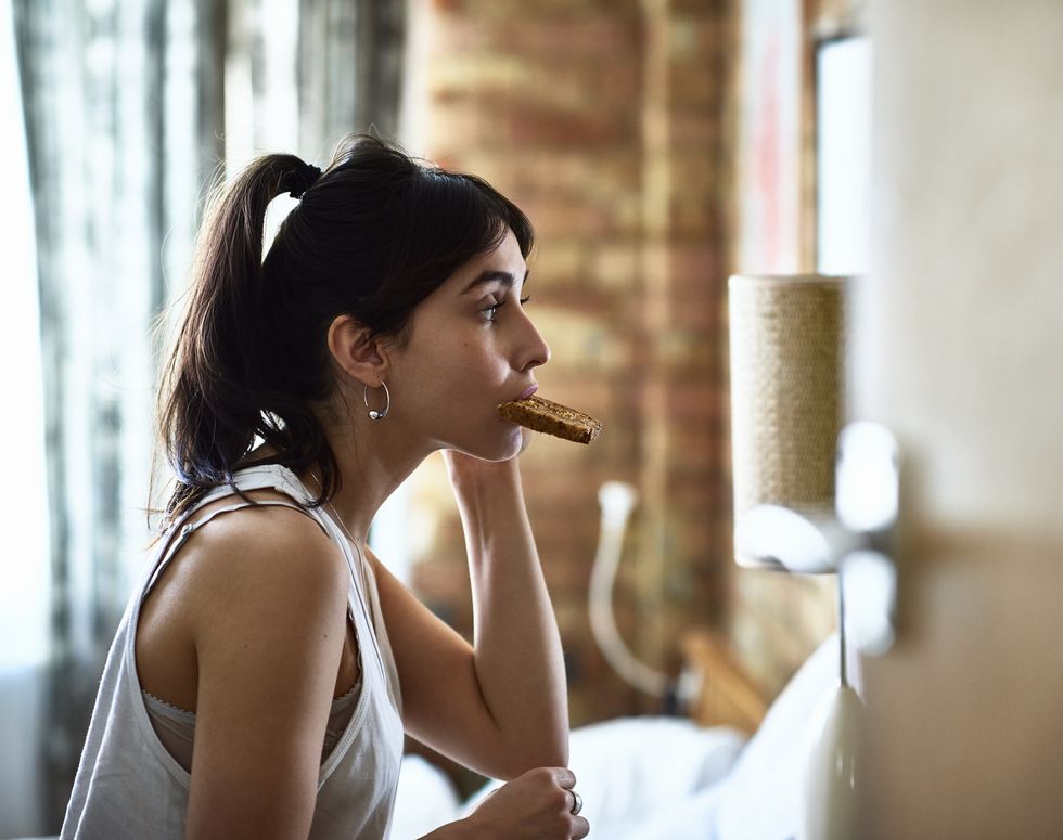 young woman biting piece of toast and checking herself in mirror