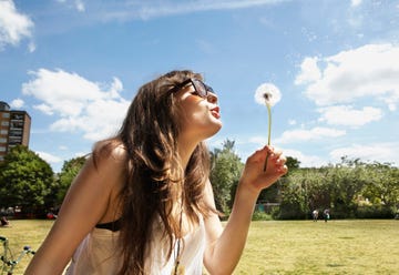 young woman blowing away the dandelion seeds