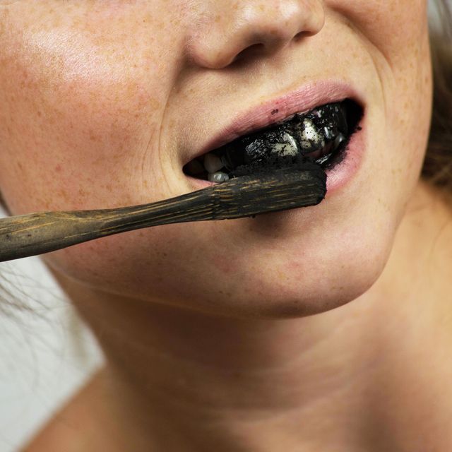 young woman brushing her teeth with a black tooth paste with active charcoal, and black tooth brush on white background for Teeth whitening