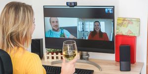 young woman chatting with friends drinking wine and laughing together   alternative party during home isolation quarantine   focus on glass hand