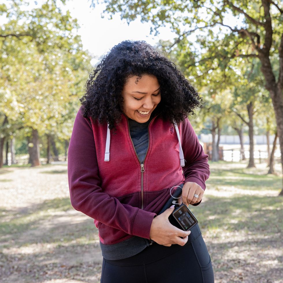 young woman checks insulin pump and blood sugar monitor while hiking outdoors