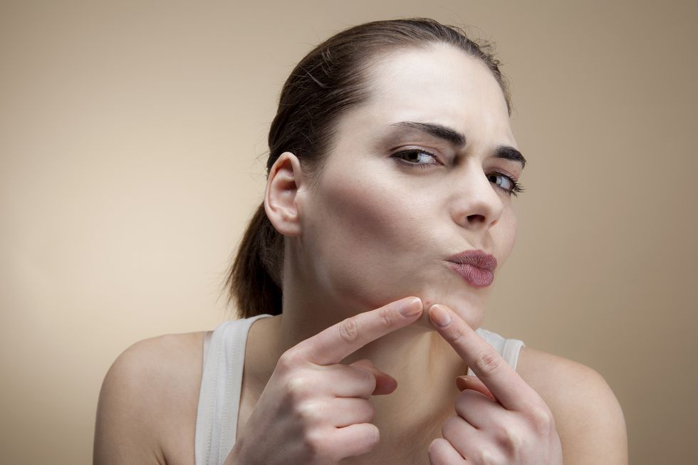 a young woman concentrating as she squeezes a pimple