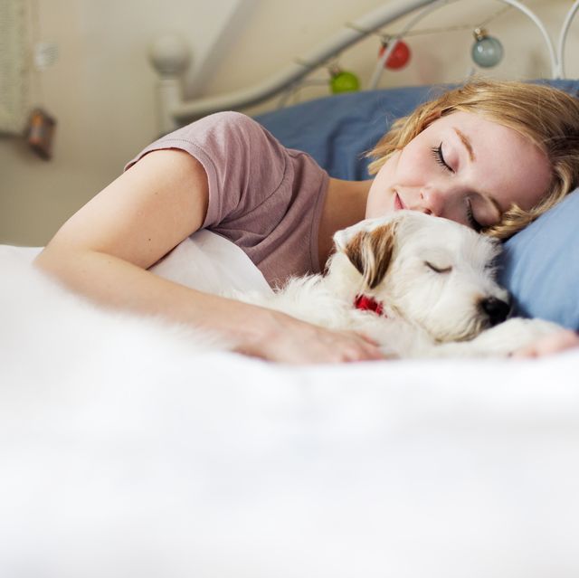 young woman cuddling up to dog in bed