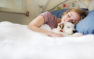 young woman cuddling up to dog in bed