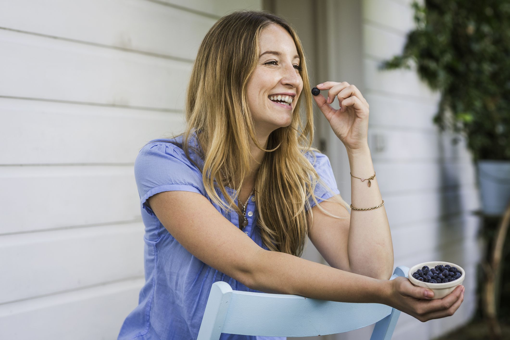 https://hips.hearstapps.com/hmg-prod/images/young-woman-eating-blueberries-in-front-porch-royalty-free-image-1690583549.jpg