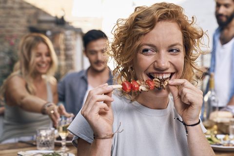 young woman eating meat skewer at a backyard patry with friends
