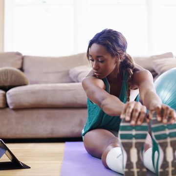 Young woman exercising on sitting room floor whilst looking at digital tablet