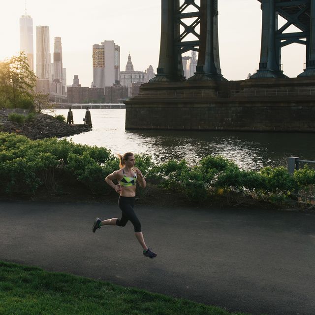 young woman exercising outdoors, running along pathway underneath brooklyn bridge, brooklyn, new york, usa