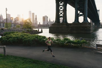 young woman exercising outdoors, running along pathway underneath brooklyn bridge, brooklyn, new york, usa
