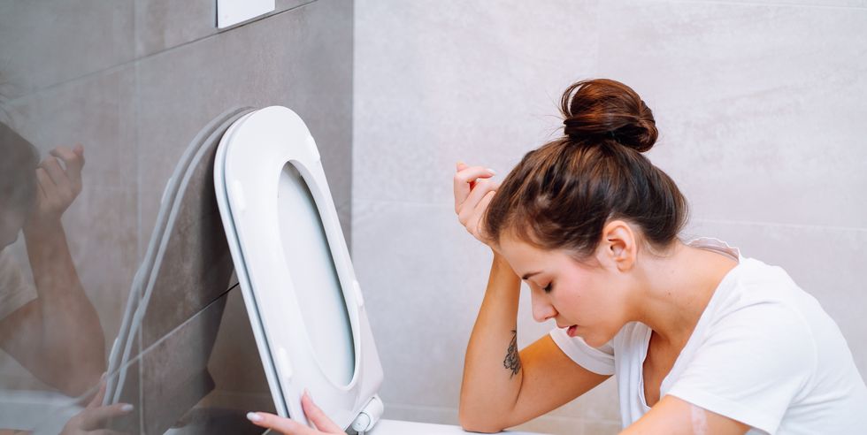 young woman feeling sick, throwing up, vomiting in toilet