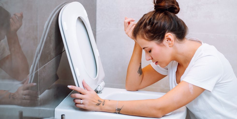 young woman feeling sick, throwing up, vomiting in toilet