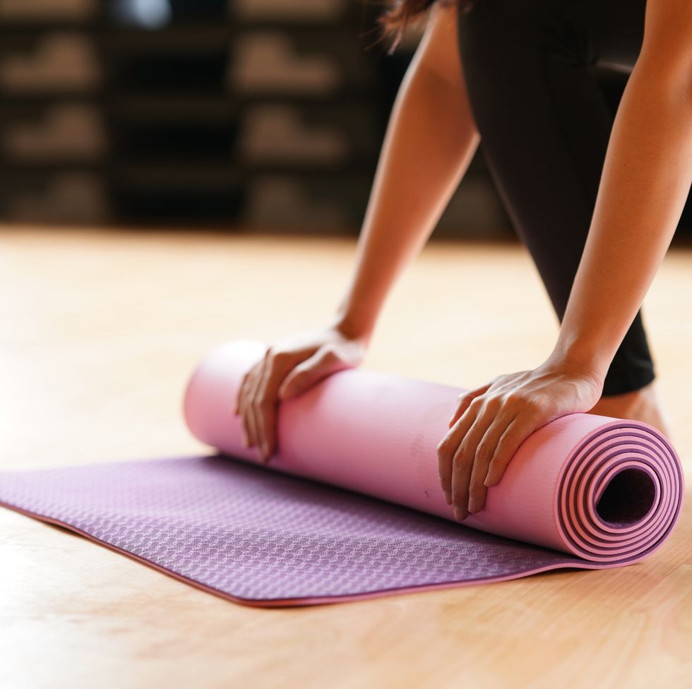 young woman folding yoga mat  after class end