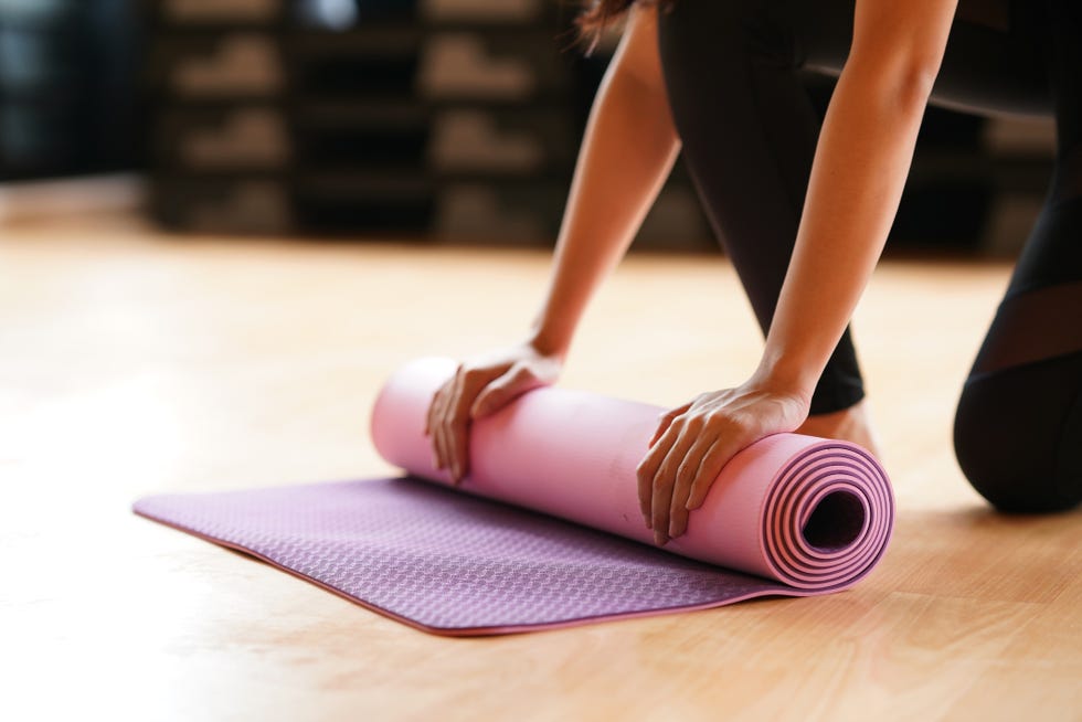 young woman folding yoga mat  after class end