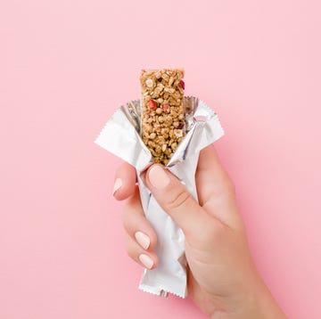 young woman hand holding cereal bar on pastel pink table opened white pack closeup sweet healthy food top view