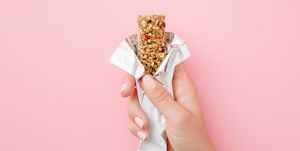 young woman hand holding cereal bar on pastel pink table opened white pack closeup sweet healthy food top view