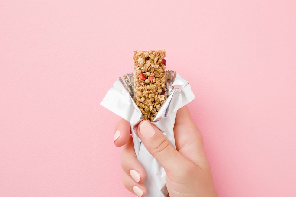 young woman hand holding cereal bar on pastel pink table opened white pack closeup sweet healthy food top view