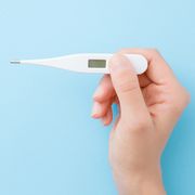 young woman hands holding white digital thermometer on pastel blue background fever and healthcare concept closeup point of view shot empty place for text top down view