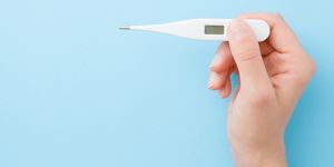 young woman hands holding white digital thermometer on pastel blue background fever and healthcare concept closeup point of view shot empty place for text top down view