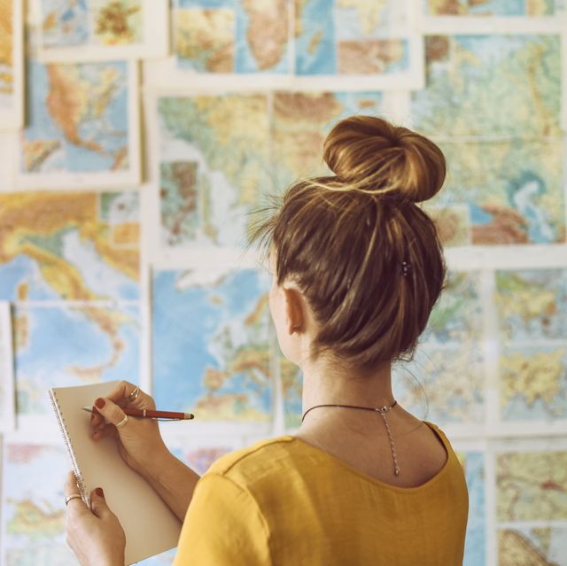 young woman handwriting at notebook while looking at map