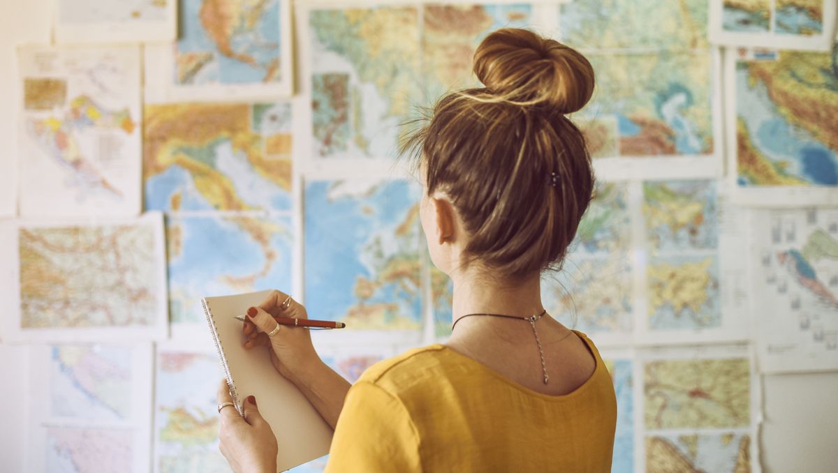 young woman handwriting at notebook while looking at map