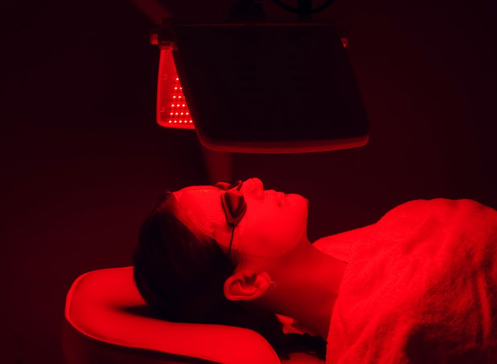 young woman having red led light facial therapy treatment in beauty salon