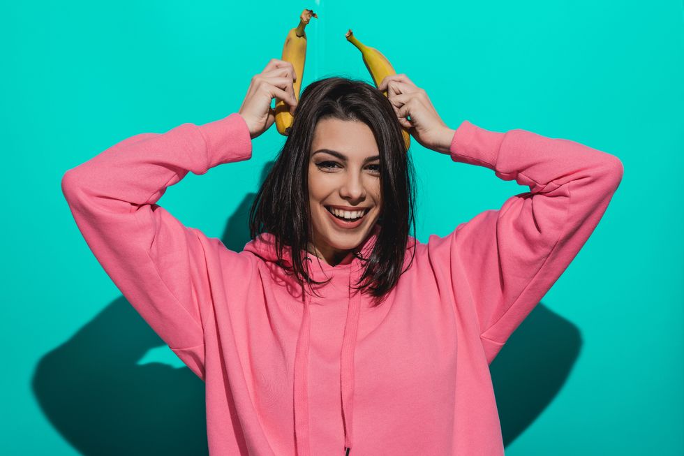 Young woman holding a banana while standing by a blue color background