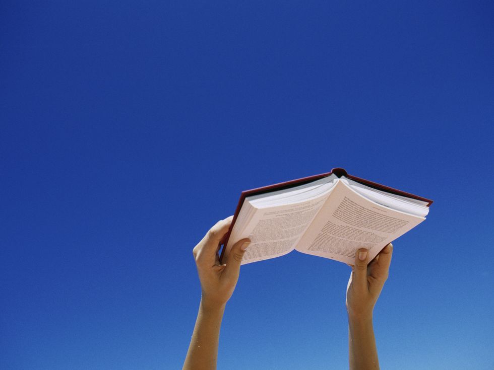 young woman holding book up in air, low angle view
