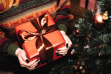 young woman holding christmas present standing by christmas tree at home