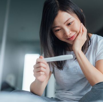 young woman holding home pregnancy test and looking happy in bedroom