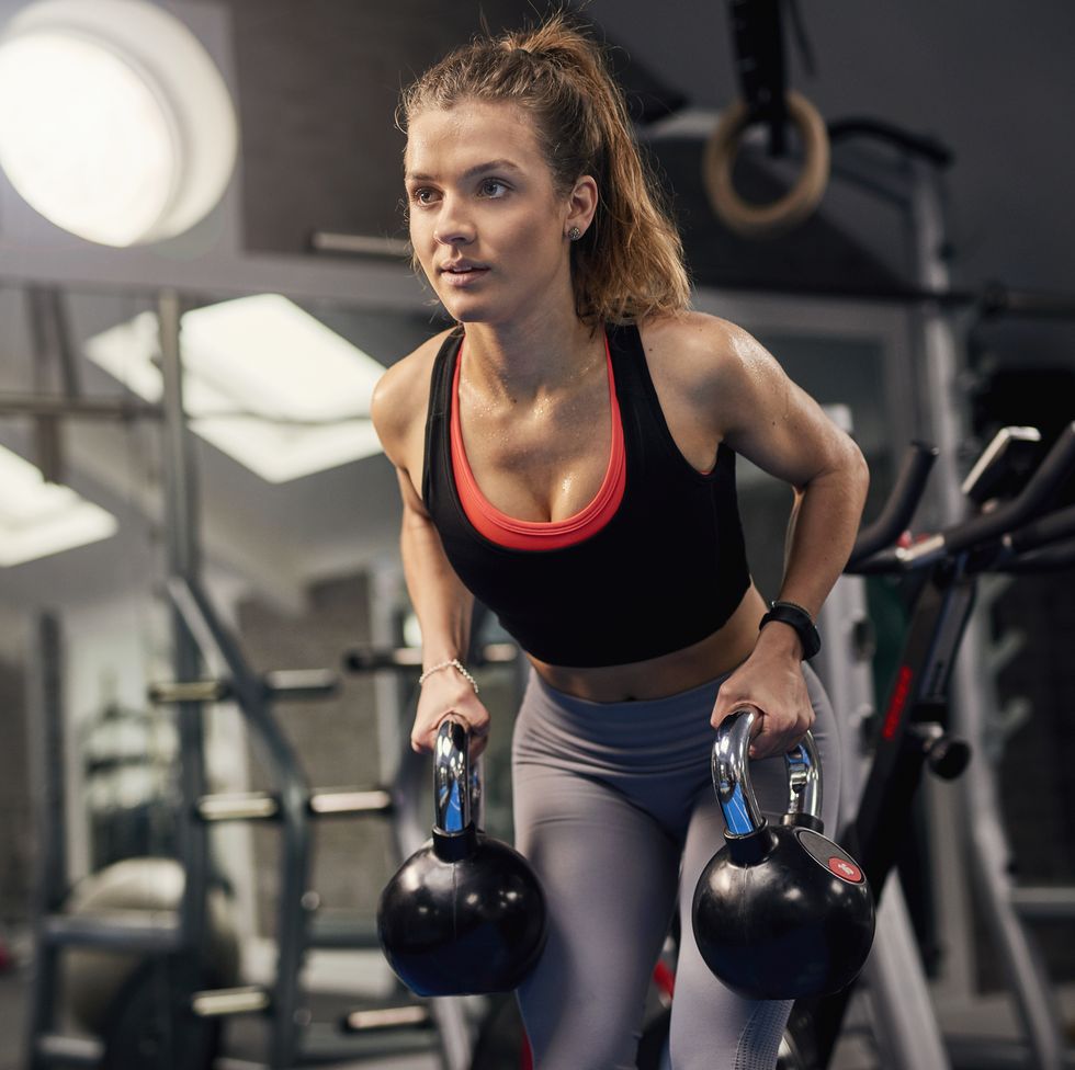 young woman holding kettle bells in gym