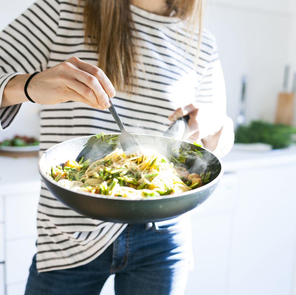 young woman holding pan with vegan pasta dish