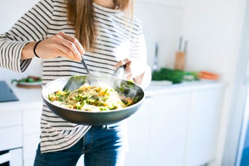 young woman holding pan with vegan pasta dish