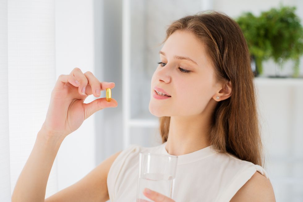 young woman holding pill omega 3 vitamin and glass of water at home, close up