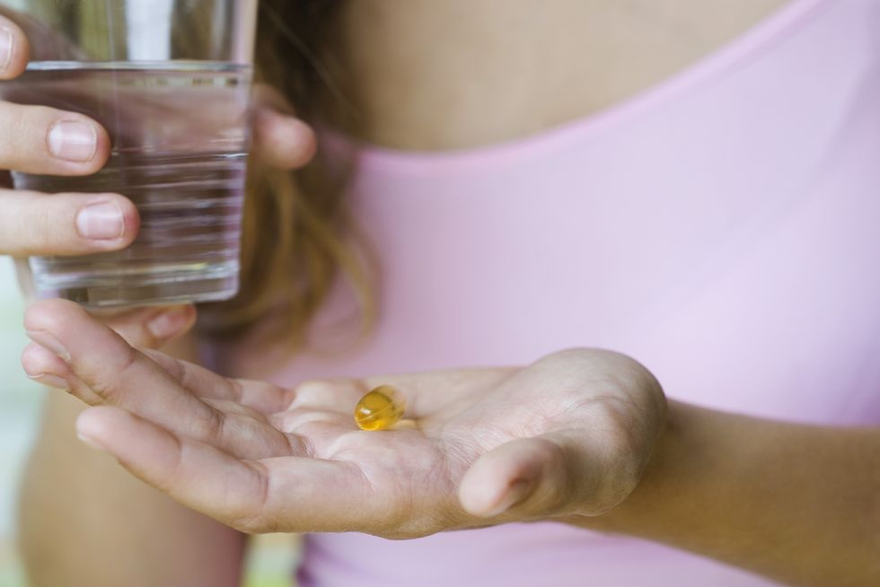 young woman holding vitamin pill and glass of water, cropped