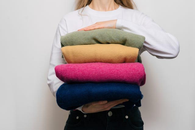 a woman holds four warm sweaters in her hands