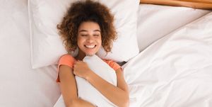 young woman hugging pillow in bed, top view