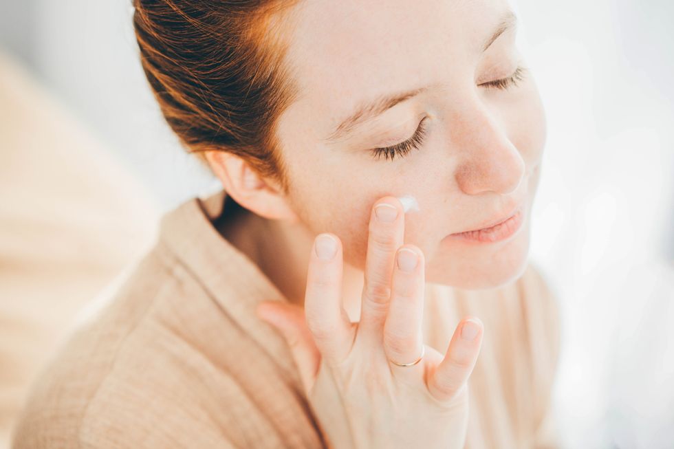 young woman in bathrobe applying moisturizing cream on face