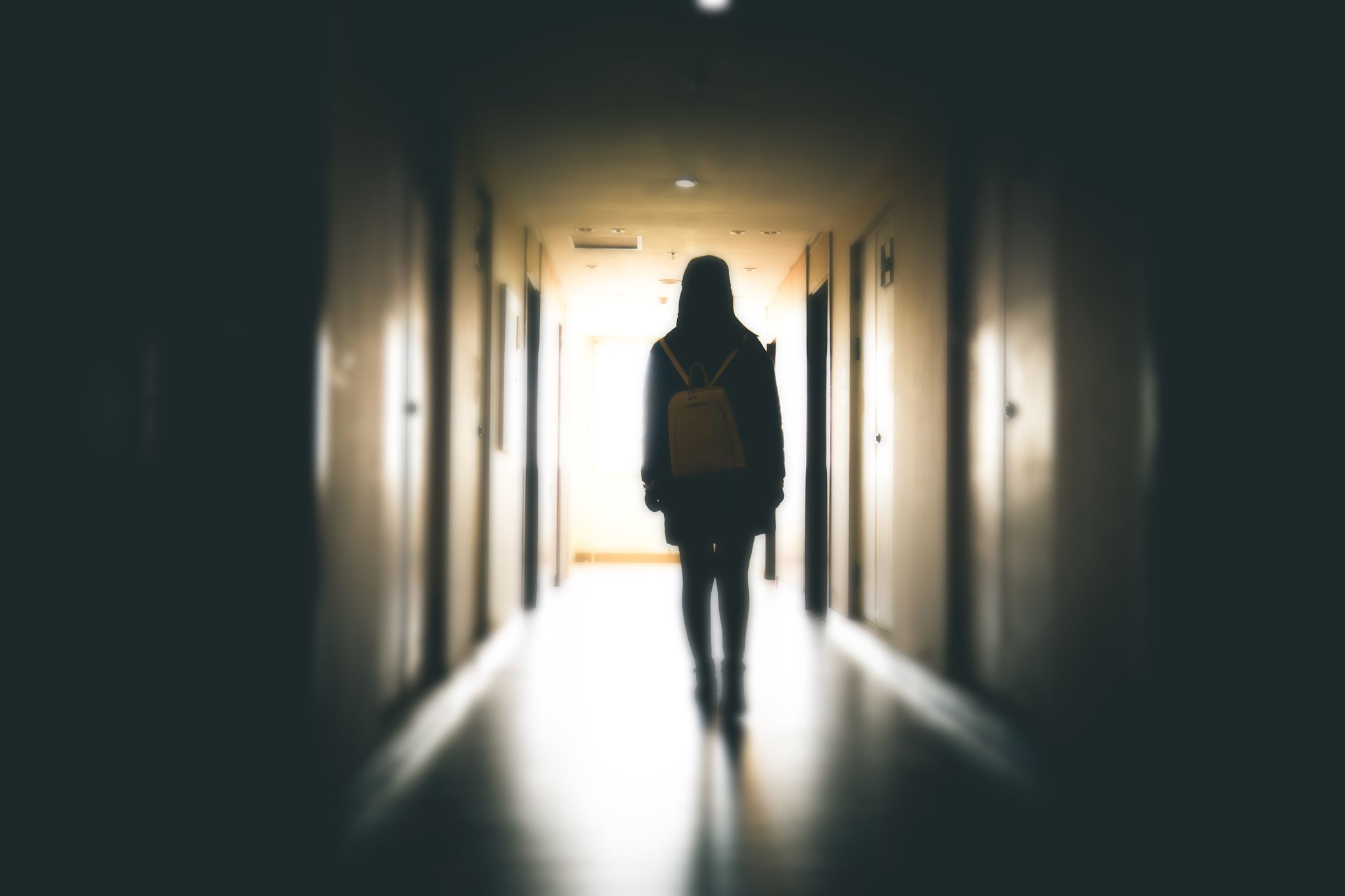 young girl walking down a dark building walkway in silhouette