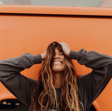 Young woman in front of orange recreational vehicle at beach, portrait, Jalama, California, USA Young woman in front of orange recreational vehicle at beach, portrait, Jalama, California, USA