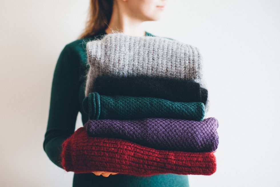young woman in green sweater holds stack of five different knitted warm winter sweaters